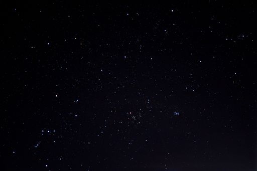 Long exposure shot capturing a luminous white streak amidst the dark night sky, accompanied by a serene moon