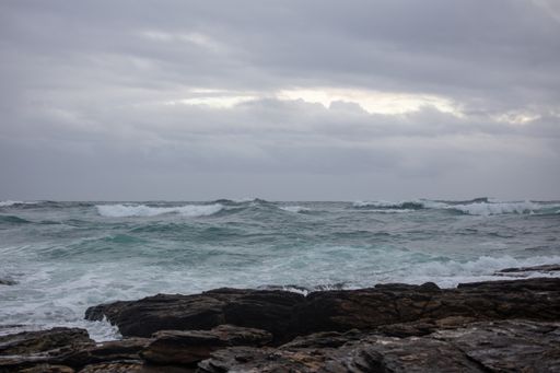 The rocks on the body of the foamy ocean under the dark cloudy sky
