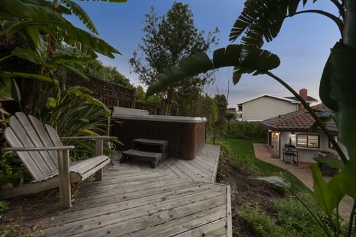 A wooden deck featuring an outdoor hot tub surrounded by lush greenery