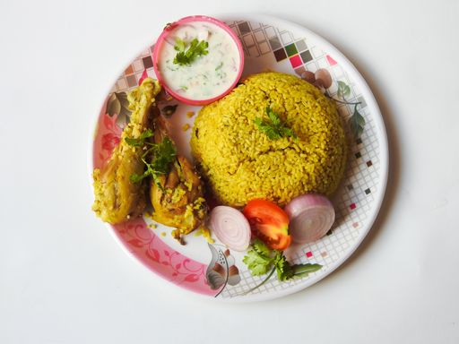A top view of a plate of delicious homemade chicken biryani and yogurt dip in a plate on a white surface