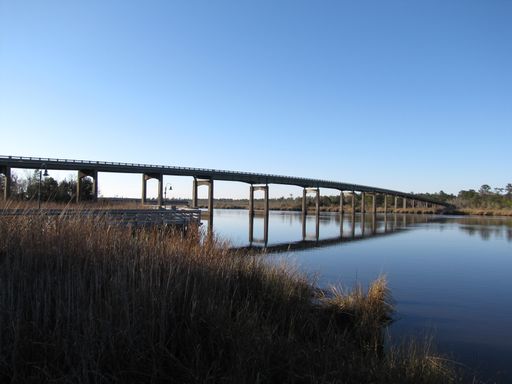 A vast bridge extends over a serene river, surrounded by lush vegetation