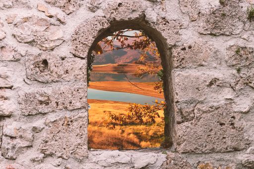 A scenic view of a tranquil lake seen through a stone arch window