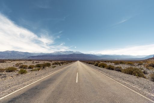 A two-lane road in an arid landscape in Argentina leading to mountains against blue sky