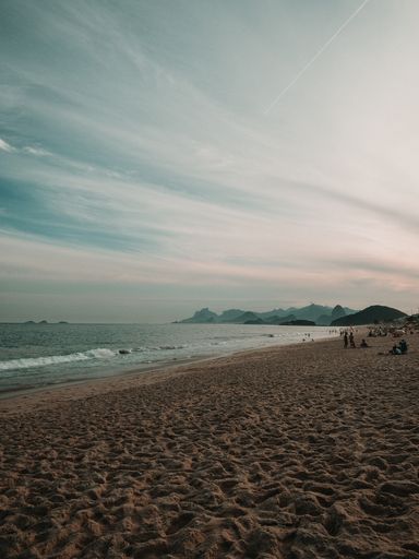 A vertical shot of a beach surrounded by the sea and hills under a cloudy sky