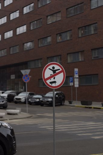 A vertical shot of a NO SKATBORDING SIGN beside a pedestrian crossing in a city