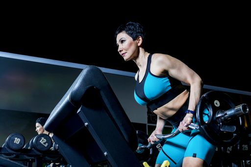 A slender middle-aged woman in a sports suit trains with a barbell in a gym. A charge of vivacity and spirit for the whole working day.