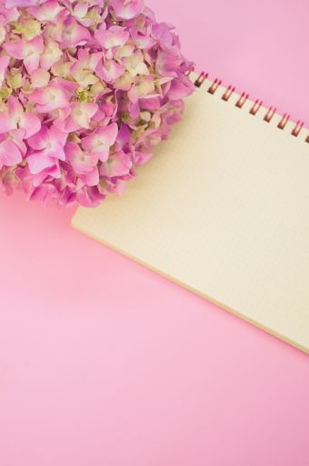 A vertical shot of a bouquet of hydrangeas with a blank notepad isolated on a pink background with space for text