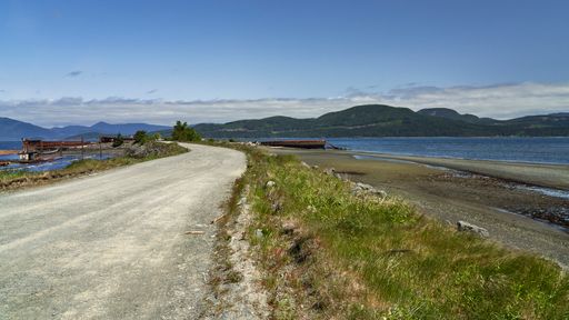 Gravel road with ocean water on both sides of it leading off into the distance.