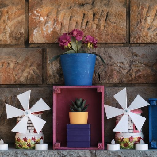 A vertical shot of plants on a pot with decorative windmills and plastic candles against brick wal
