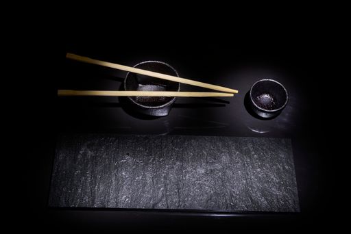 A top view of a black wooden board and sushi chopsticks on a black background