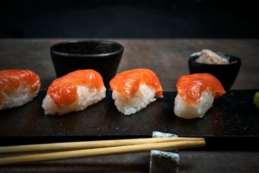 A closeup shot of sushi on a black wooden board with chopsticks on a blurred background