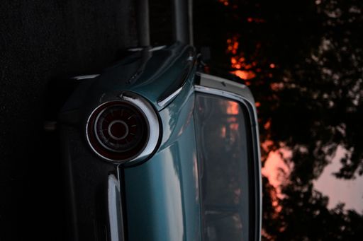 A vintage car parked in front of a picturesque sunset, framed by majestic trees