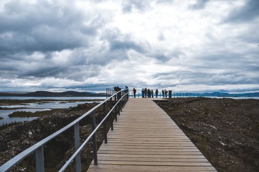 A long shot of a boardwalk with railing and tourists, overlooking a lake on a cloudy day
