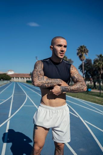 A man with tattoos standing on a sunny track with palm trees in the background