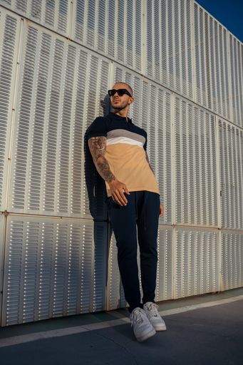 A young man posing outdoors on a sunny day wearing sunglasses against a metal wall