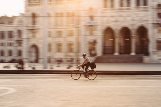 A man riding a bike in front of the Budapest parliament building during sunset with a panning effect