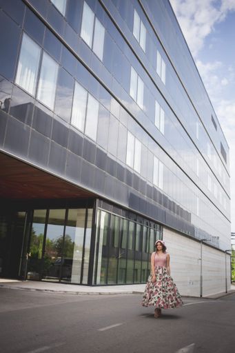 A vertical shot of a young woman standing in front of a modern building in a pink dress
