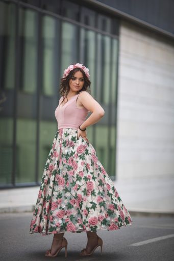 A vertical shot of a Caucasian standing in front of a modern building in a pink dress and hairband