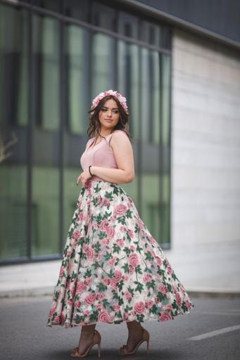 A vertical shot of a woman standing in front of a modern building in a pink dress