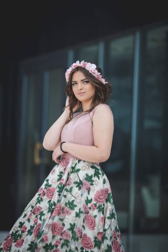A closeup shot of a woman standing in front of a modern glassed building in a pink dress