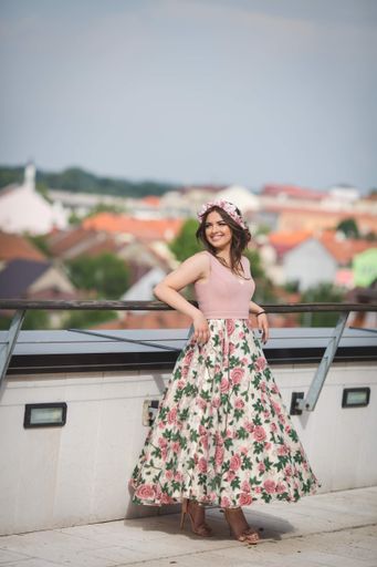 A shallow focus shot of a woman standing on a roof a pink dress and smiling