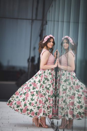 A vertical shot of a young woman in a pink dress and her reflection on a glass wall