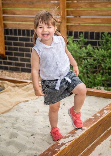 Young girl playing outdoors, balancing on one leg in a sandbox