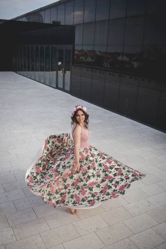 A pretty Caucasian woman with a floral skirt dancing and rotating in front of a restaurant building