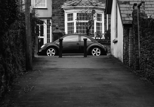 A black Volkswagen Beetle parked in front of a charming small building, in grayscale