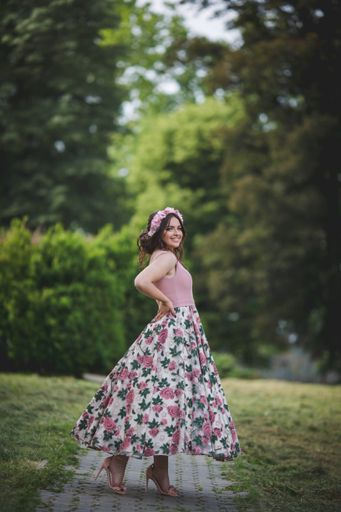 A vertical shot of a smiling caucasian female in a romantic dress with flowers standing on a pathway in a park