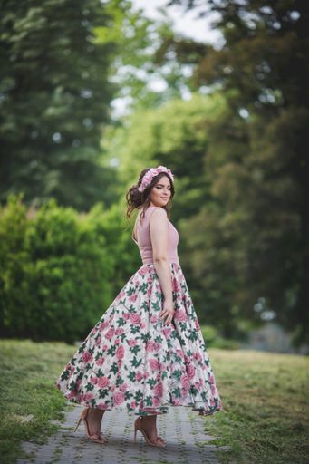 An attractive Caucasian female wearing an elegant long floral dress posing in the park