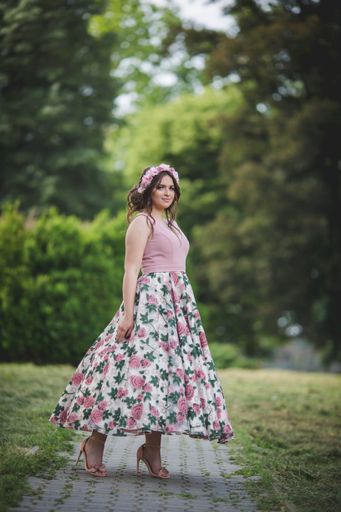 An attractive Caucasian female wearing an elegant long floral dress on background of a park