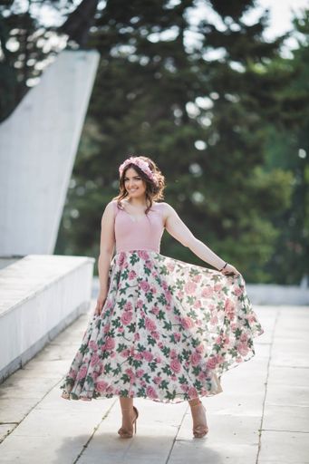 An attractive Caucasian female wearing an elegant long floral dress posing in a park