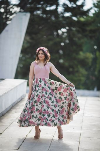 An attractive Caucasian female wearing an elegant long floral dress posing in a park