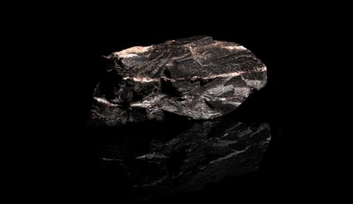A close-up shot of unprocessed manganese ore rock on a reflective black background