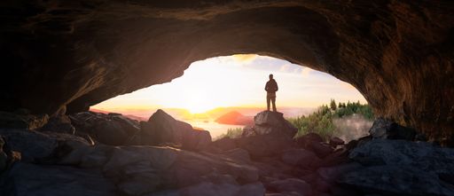 A man standing at the entrance of the cave admiring the vibrant sunset