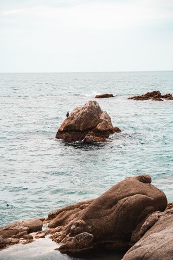 A vertical shot of a rocky seashore in the wavy sea at daylight