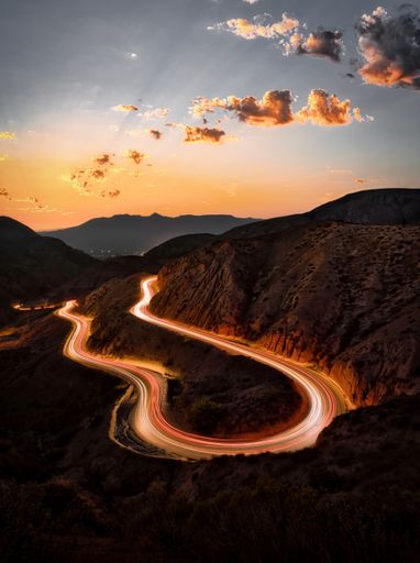 A vertical long exposure shot of a road in the mountains under a sunset sky