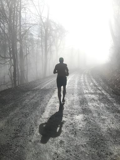 A grayscale of a runner running up a mountain on a dirt road in the fog