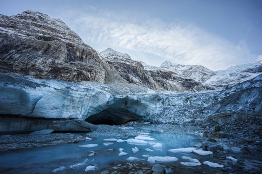 Winter landscape view of a glacier ice cave entrance surrounded by mountains and small icebergs