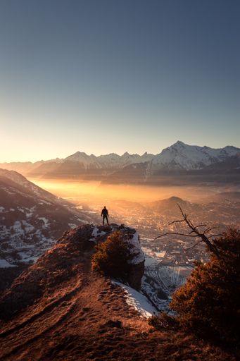 Winter landscape view of a silhouette standing on a rock over a foggy valley illuminated by the setting sun