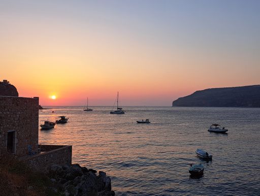 A scenic view of multiple small boats in a serene bay near a rustic structure