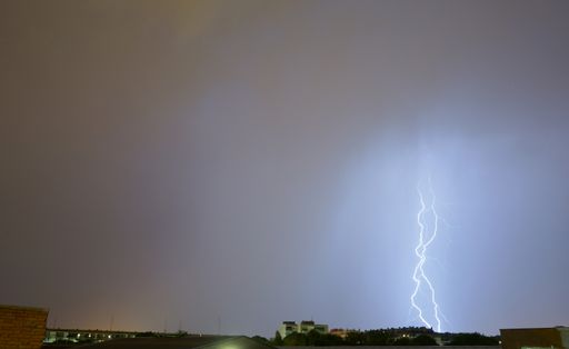 Spectacular storm and lightning illuminates the sky and strikes one of the buildings in a city. Torrejon de Ardoz.