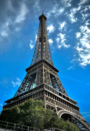 The Eiffel Tower under blue cloudy sky with trees in front