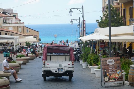 Shopping street of Tropea, Calabria in Italy. Typical three wheels small delivery car heading towards Mediterranean sea.