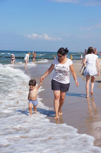Woman and a small child walking on sand close by the water at a beach on a sunny day.