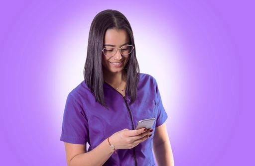 A cheerful young Hispanic doctor/nurse wearing glasses using her smartphone