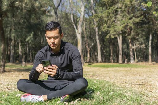 Fit young latino man in sportswear standing in the middle of the forest checking his sports watch