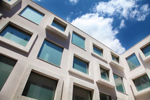 A low angle shot of a modern building with glass windows under a cloudy blue sky