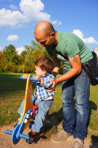 An unidentified man standing next to a boy on a spring swing on a sunny day